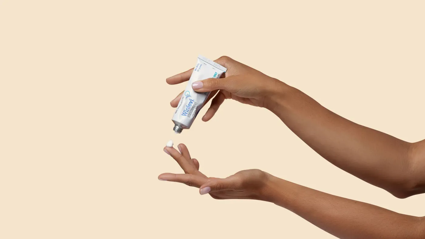 A hand applying Winlevi skincare cream at a bathroom sink, showing the product in real, everyday use.