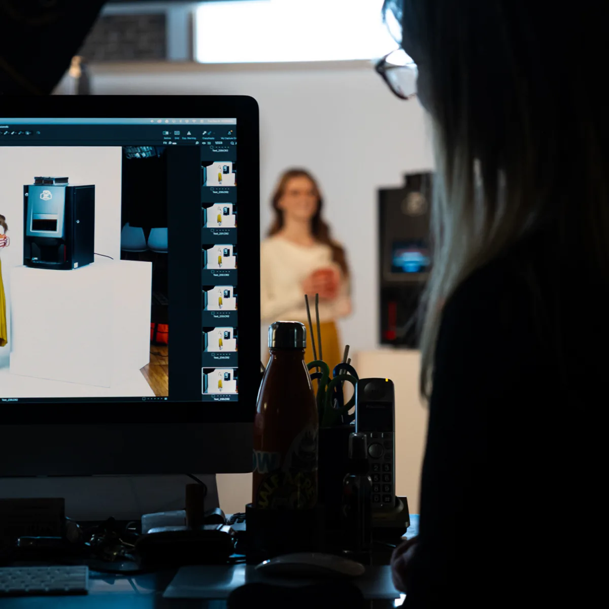 Over-the-shoulder view of a team member reviewing just-captured images of a WithMe coffee machine on a studio monitor, with a model on set in the background